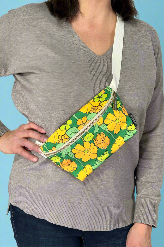 Model is wearing a retro green floral printed fanny pack bag with an adjustable canvas strap. 