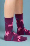 Purple socks with pink dinosaur pattern worn by a person on a white background