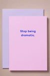 A light pink greeting card with blue text that reads ‘Stop being dramatic.’