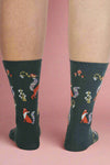 Dark blue socks with fox and flower pattern worn by a person on a light gray background