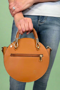 Model is carrying a small circle purse with braided handle, gold keychain and exterior pockets. Includes a cross body strap. 