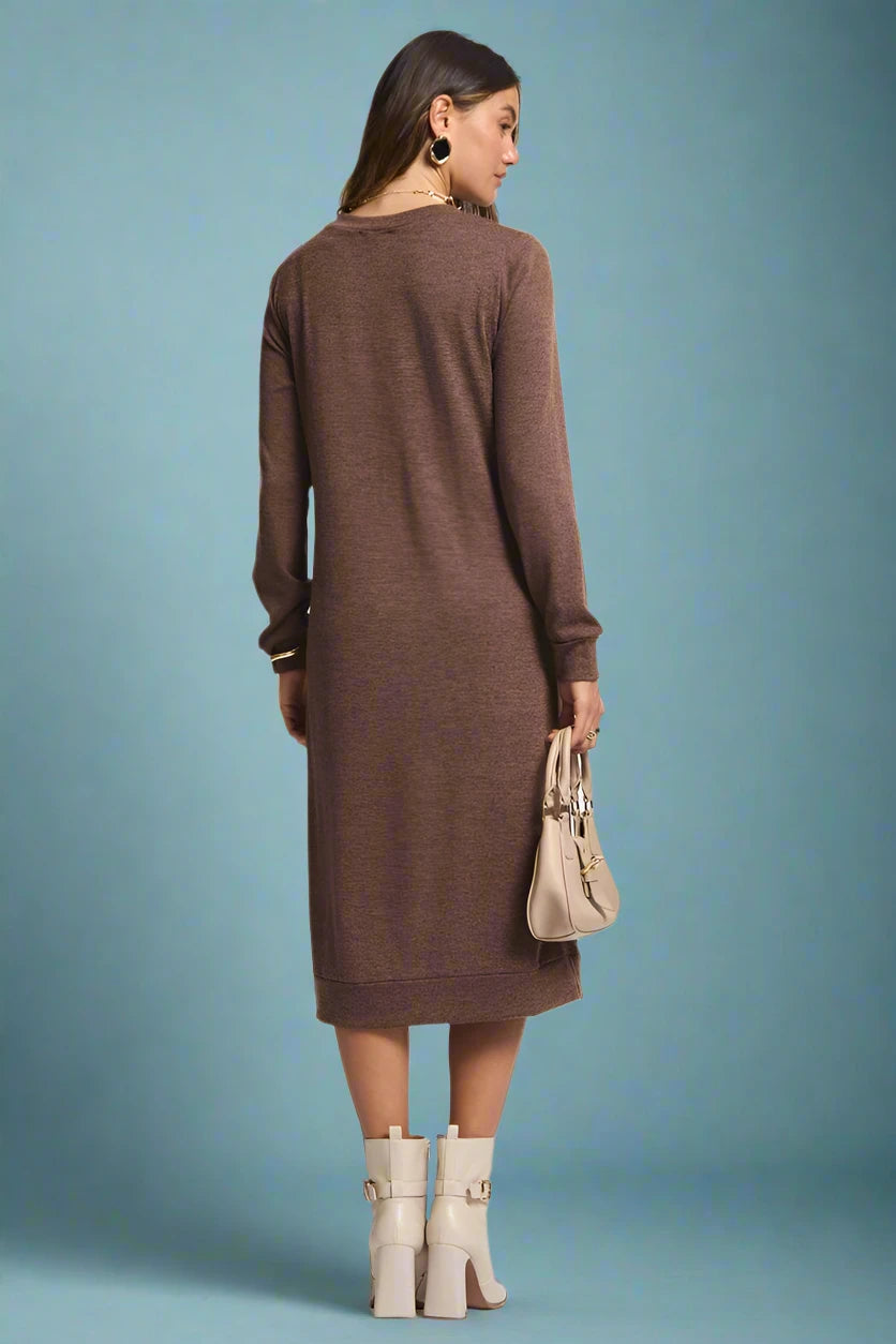 Woman wearing a brown dress with beige boots and a handbag on a plain background
