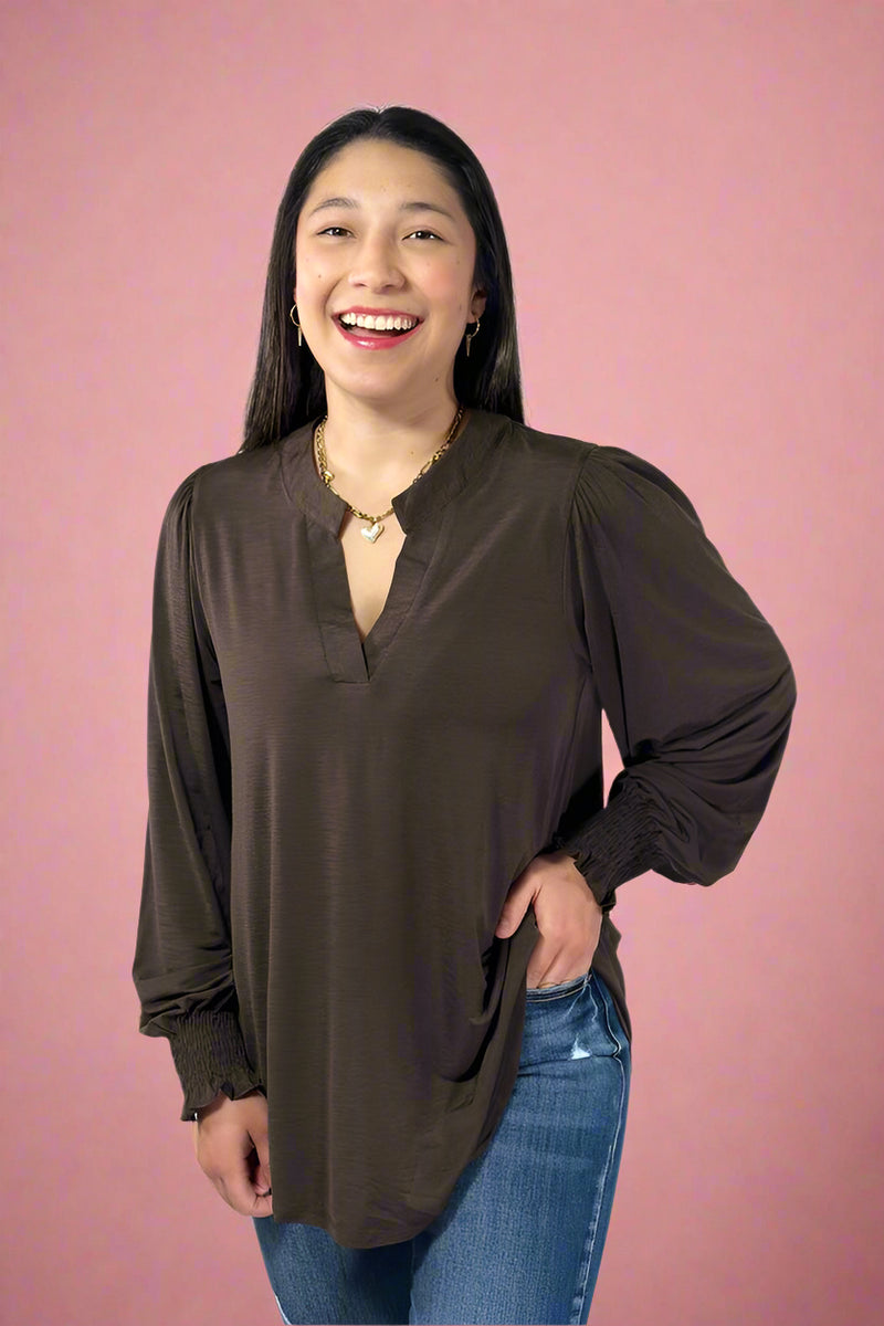 Woman wearing a brown blouse and blue jeans against a plain background.