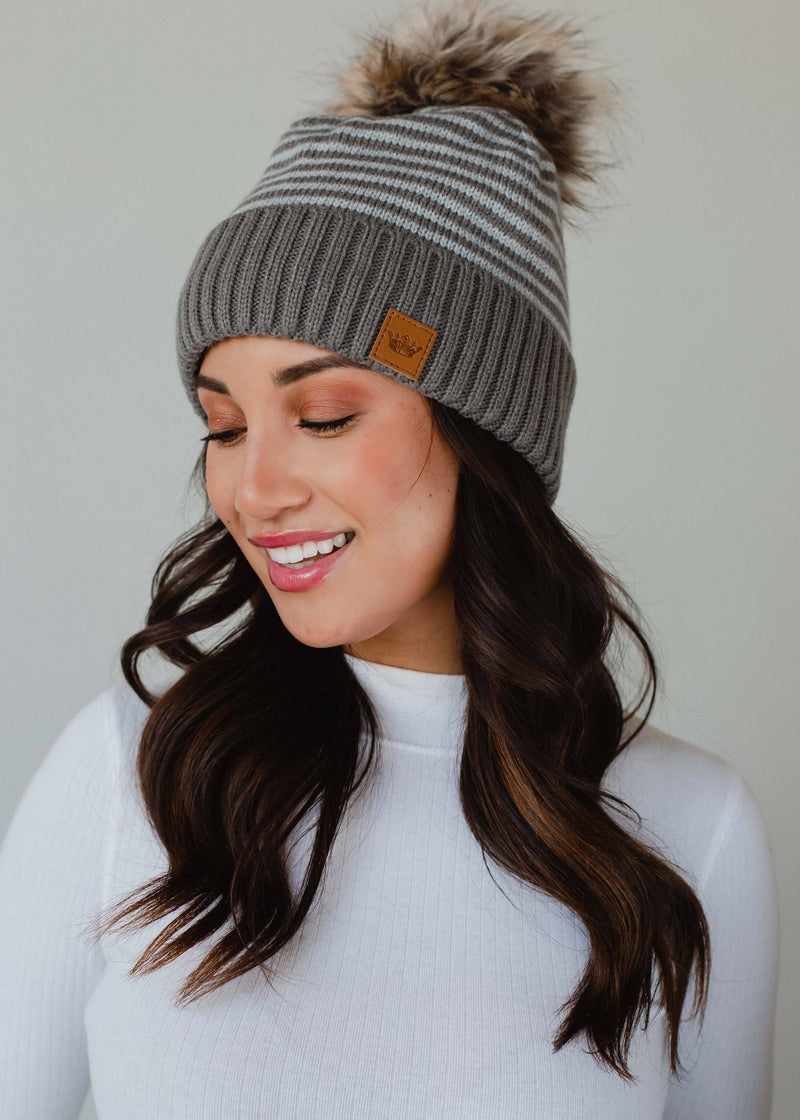 Woman wearing a gray knit beanie with a pom-pom on a plain background