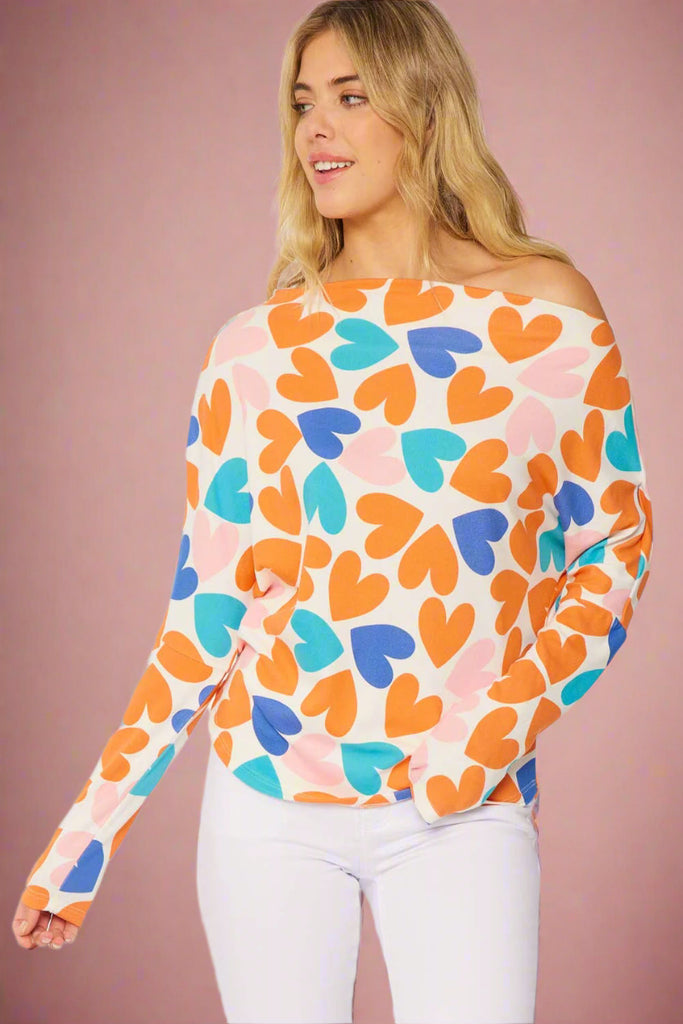 Model is wearing a white long sleeve boat neck top with colorful hearts all over. 