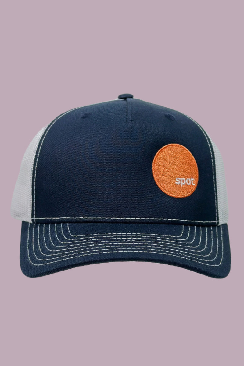 Navy colored trucker hat with white mesh back and contrasting stitching, featuring an embroidered Spot logo.