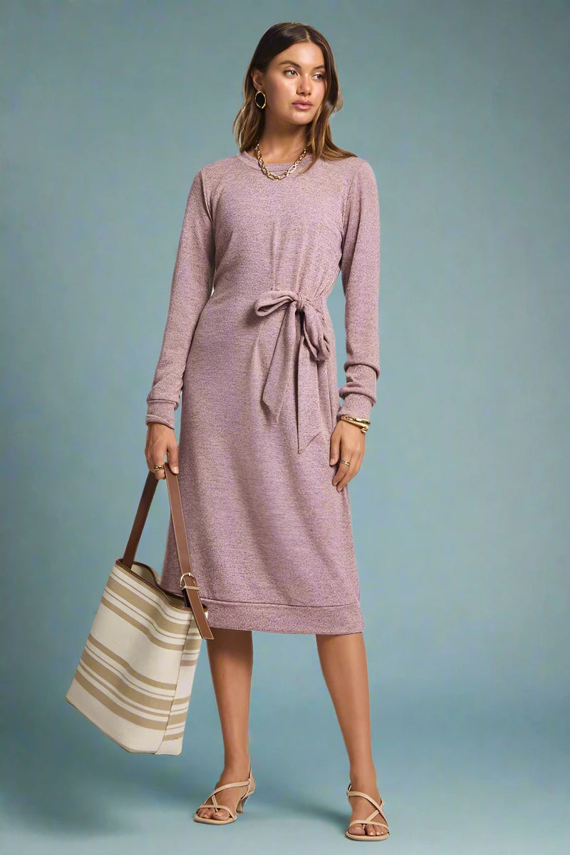 Woman wearing a pink dress holding a striped bag on a plain background