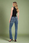 Woman wearing blue jeans and a black top on a plain background.