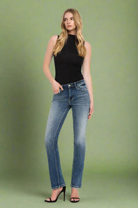 Woman wearing blue jeans and a black top on a green background.