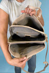 Model is wearing a large natural colored satchel with multiple compartments. 