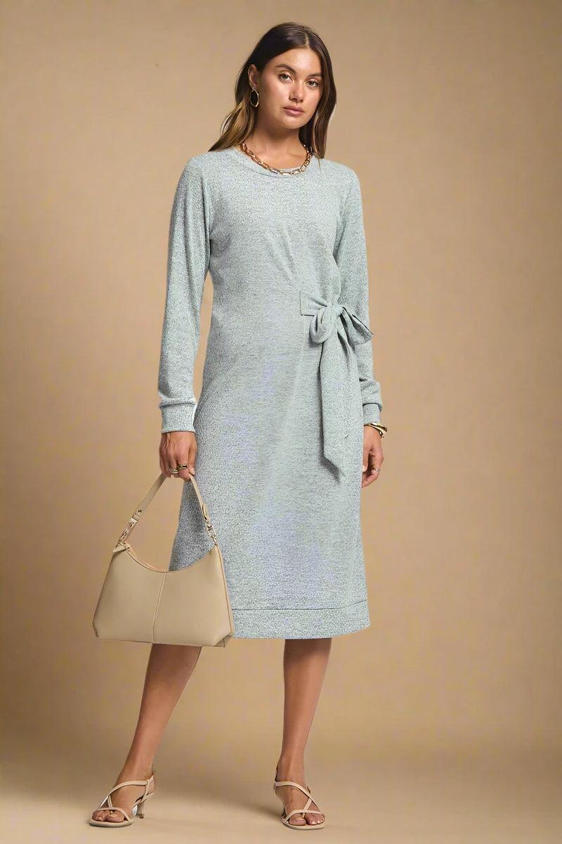 Woman wearing a gray dress holding a beige handbag on a plain background