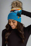 Woman wearing a blue beanie with a mountain design against a gray background