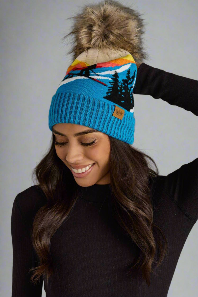Woman wearing a blue beanie with a mountain design against a gray background
