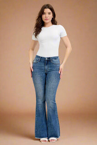 Woman wearing a white t-shirt and blue flared jeans on a plain background.