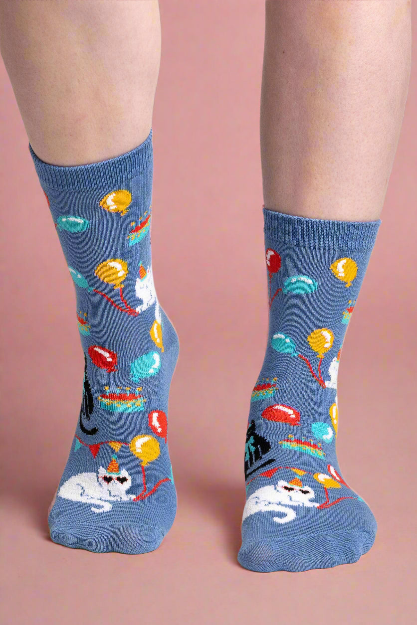 Blue socks with colorful balloon and cat pattern worn by a person on a white background
