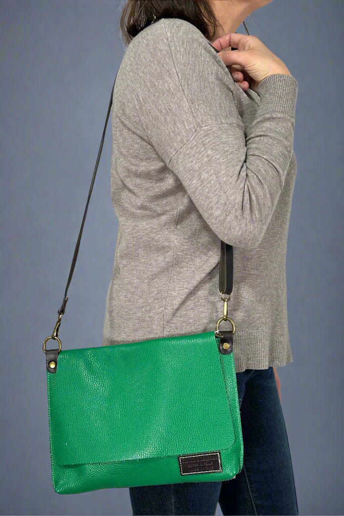 Model is wearing a kelly green colored crossbody bag with an adjustable strap. 