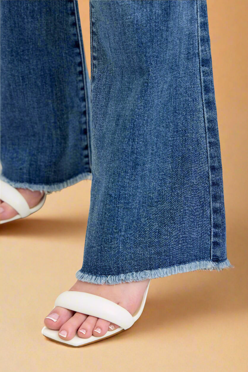 Close-up of blue jeans with a white sandal on a light background.