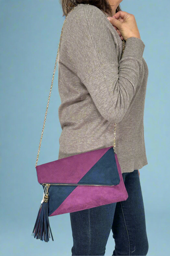 Model is wearing a purple and navy color blocked crossbody with a delicate chain strap and large tassel. 