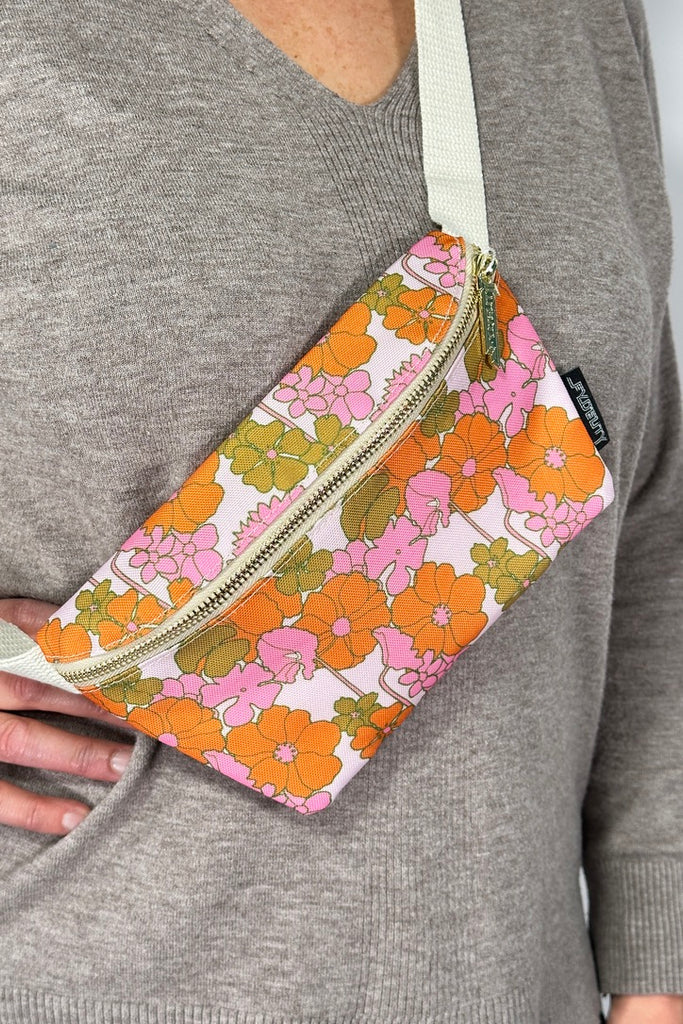 Model is wearing a retro pink floral printed fanny pack bag with an adjustable canvas strap. 