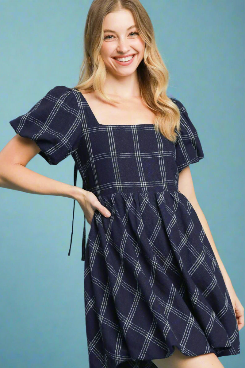 Model is wearing a plaid navy and white dress with puff sleeves.