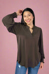 Woman wearing a brown long-sleeve top and blue jeans against a white background