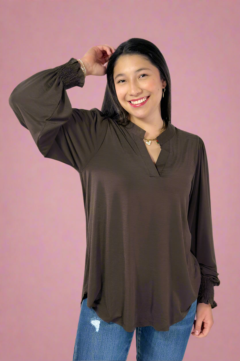 Woman wearing a brown long-sleeve top and blue jeans against a white background