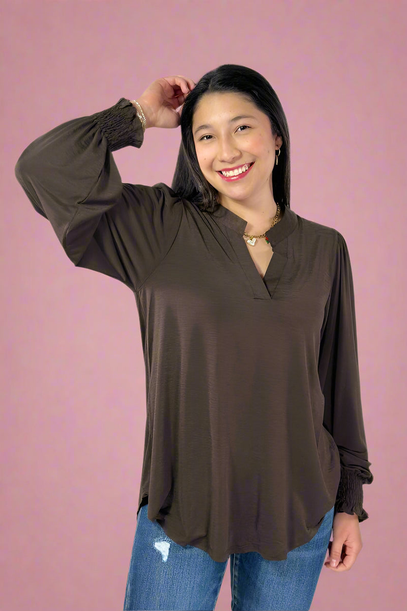 Woman wearing a brown long-sleeve top and blue jeans against a white background
