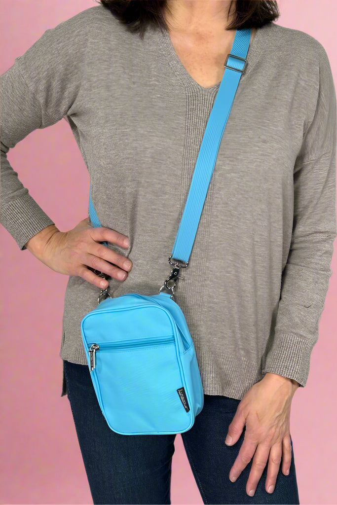 Model is wearing a small neon blue crossbody bag with an external zipper pocket and adjustable canvas strap. 