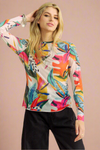 Model is wearing a sheer crew neck long sleeve top featuring a vibrant tropical print.