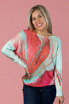 Model is wearing a light knit sweater with dolman sleeves and a vibrant coral and teal print.