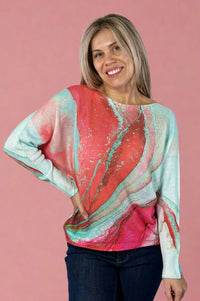 Model is wearing a light knit sweater with dolman sleeves and a vibrant coral and teal print.