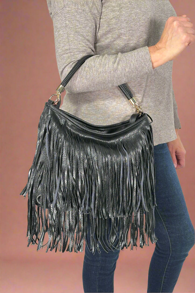 Model is holding a black purse with layers of faux leather fringe. 