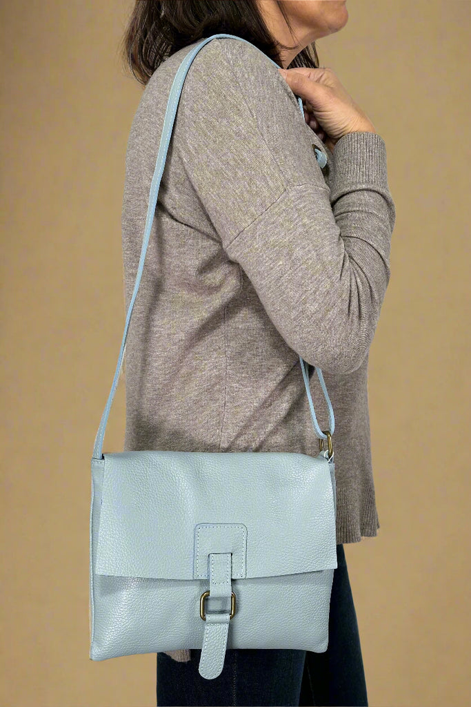 Model is wearing a sky blue colored flap crossbody bag. 