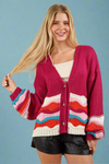 Model is wearing an oversized chunky knit cardigan with bell sleeves and a colorful wave pattern. 