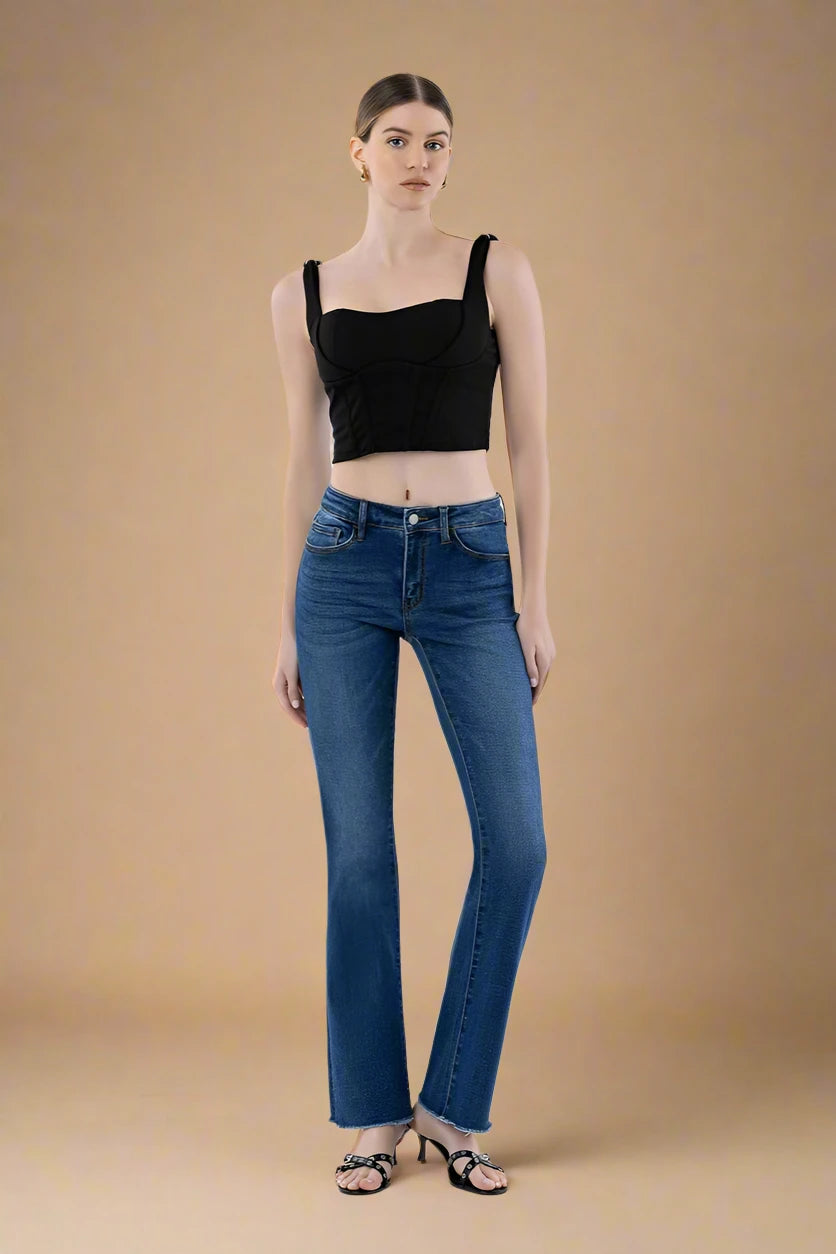 Woman wearing a black crop top and blue jeans on a plain background.
