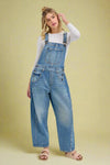 Woman wearing blue denim barrel leg overalls on a white background