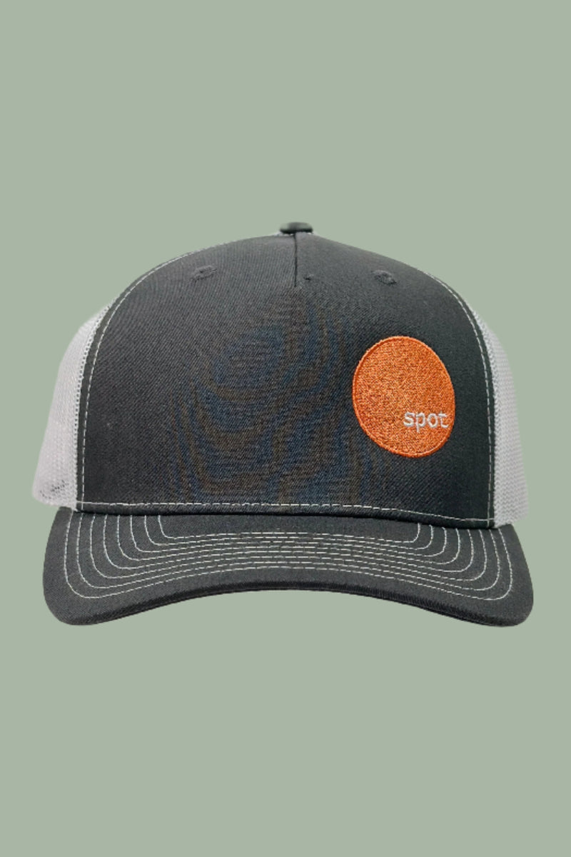 Charcoal grey colored trucker hat with a white mesh back and contrasting stitching featuring an embroidered Spot logo.