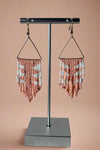 Triangle shaped dangly earrings that feature peach and white colored bead detailing.