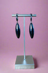 Brushed black colored mini hoop earrings with a large oval pendant attached.