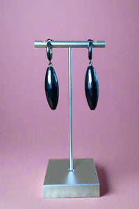 Brushed black colored mini hoop earrings with a large oval pendant attached.