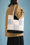 Models holds adorable, canvas shoulder bags featuring a modern, blocky, checkered plaid with light blue, navy, and sage accents.