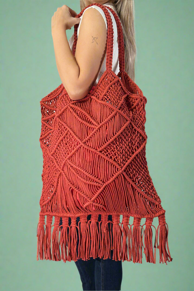 Model is wearing an oversized red cotton macrame tote bag with fringe detailing.