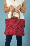 Model is holding a red cotton macrame bag with wooden top handles. 