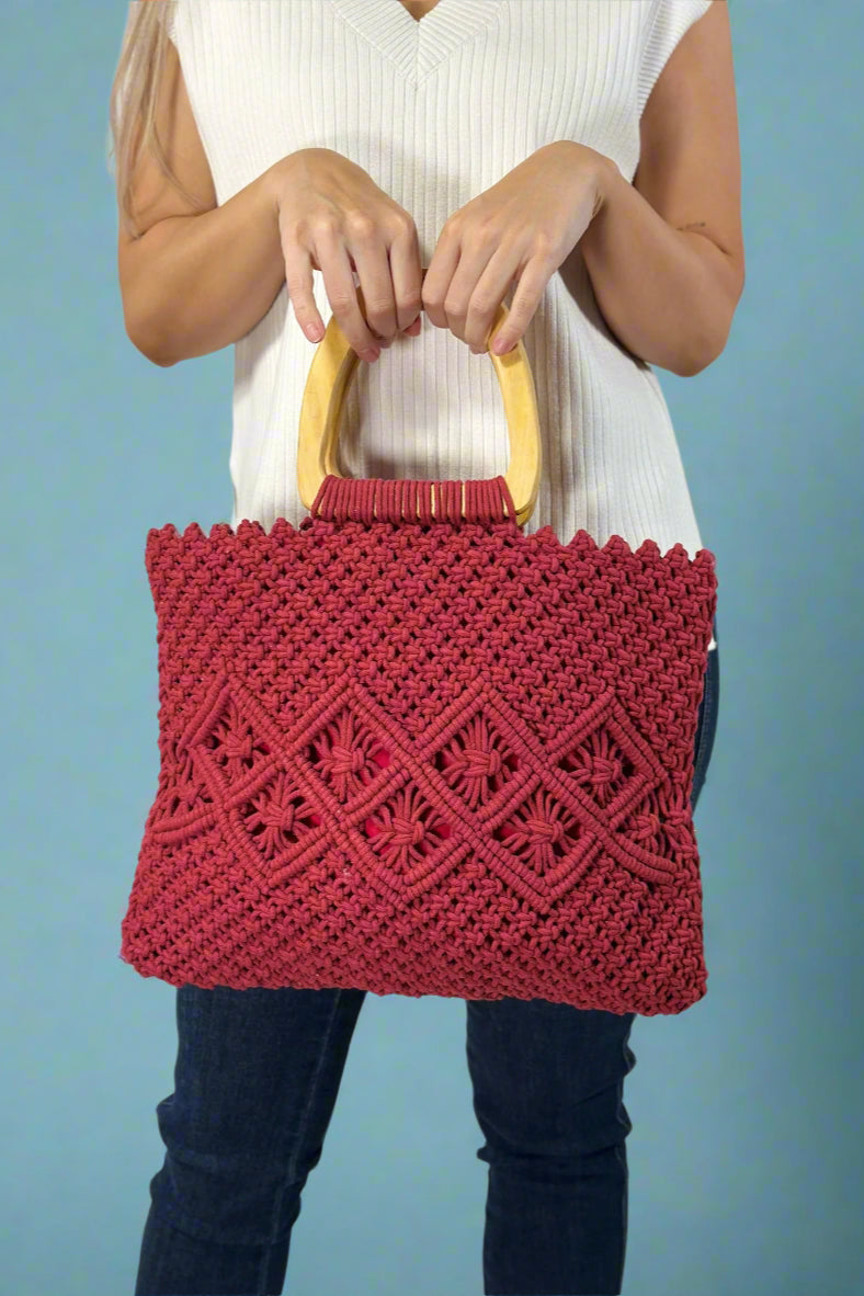 Model is holding a red cotton macrame bag with wooden top handles. 