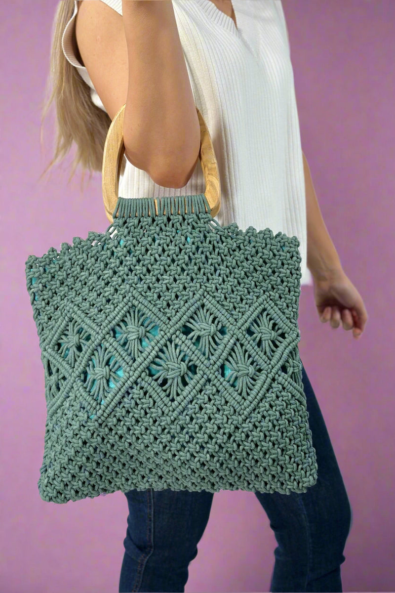 Model is holding a green colored cotton macrame purse with wooden top handles.