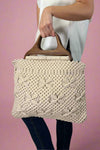 Model is holding a beige colored cotton macrame purse with dark wooden top handles. 