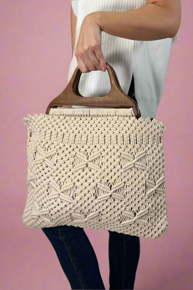 Model is holding a beige colored cotton macrame purse with dark wooden top handles. 