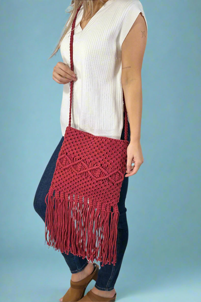 Model is wearing a red cotton macrame sling bag with fringe detailing. 