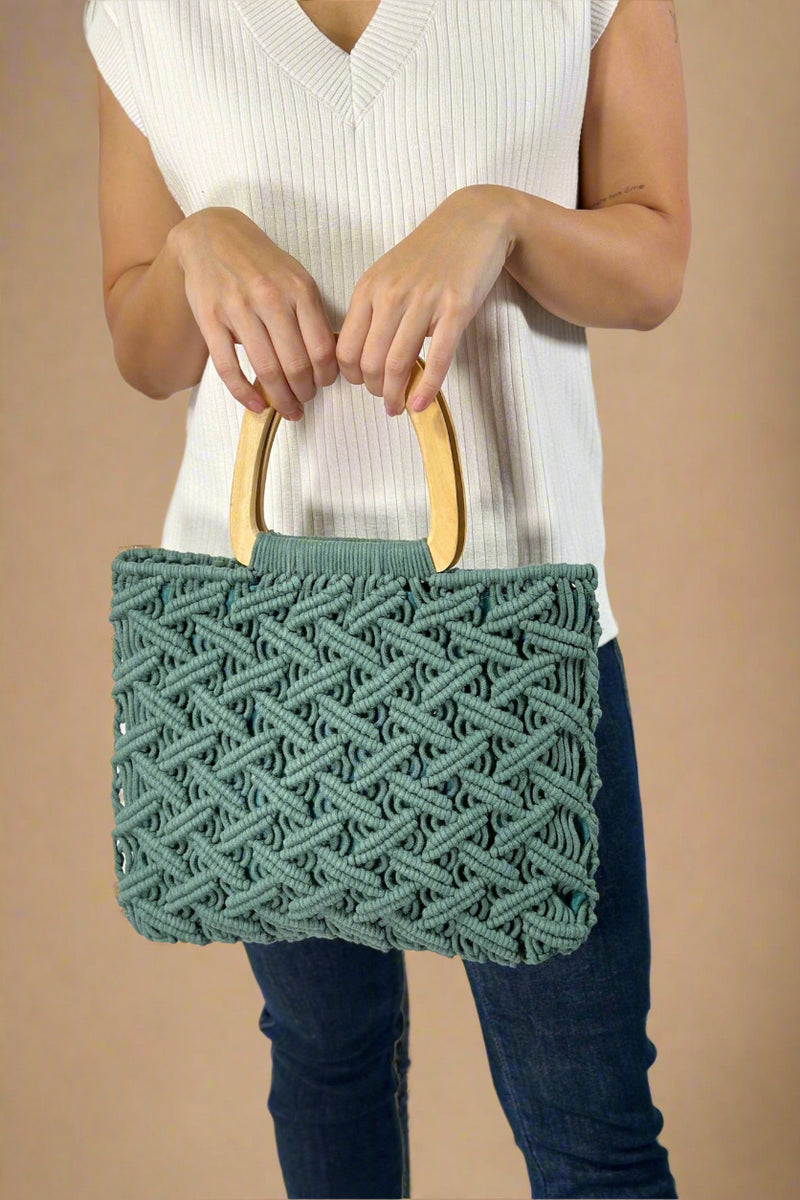 Model is holding a green colored cotton macrame purse with wooden top handles. 