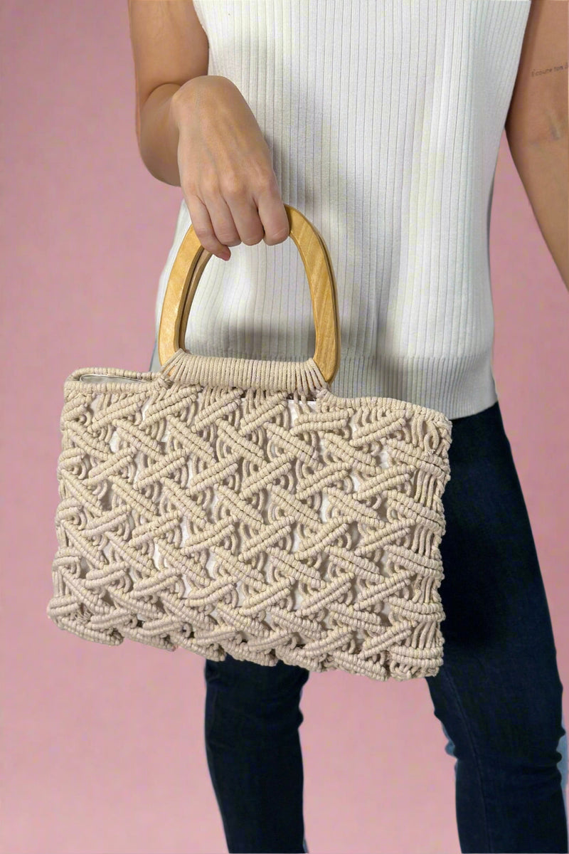 Model is holding a beige colored cotton woven macrame purse with wooden top handles.
